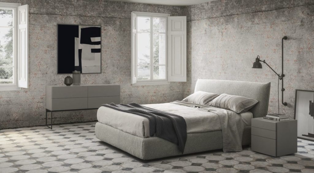 Vista general de una amplia habitación en tonos grises amueblada con una moderna cama, una cajonera y una mesita de noche