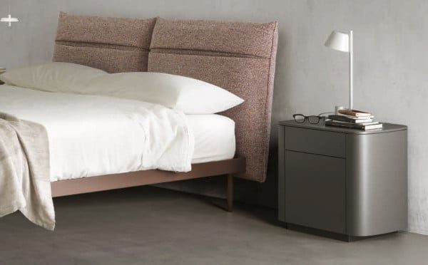 Exclusiva cama con compartimentos en su respaldo acompañada de un aparador en color gris realizando la función de mesita de noche